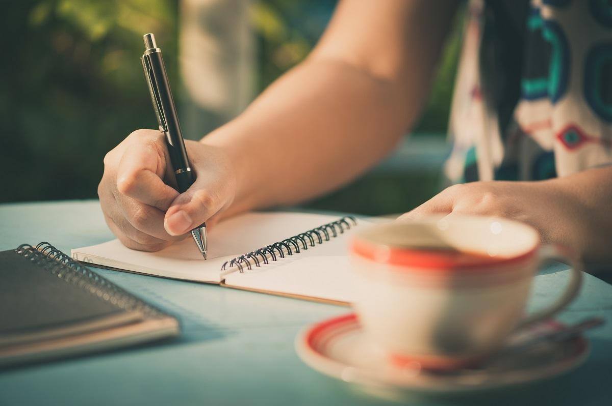 woman writing in notebook beside cup of coffee