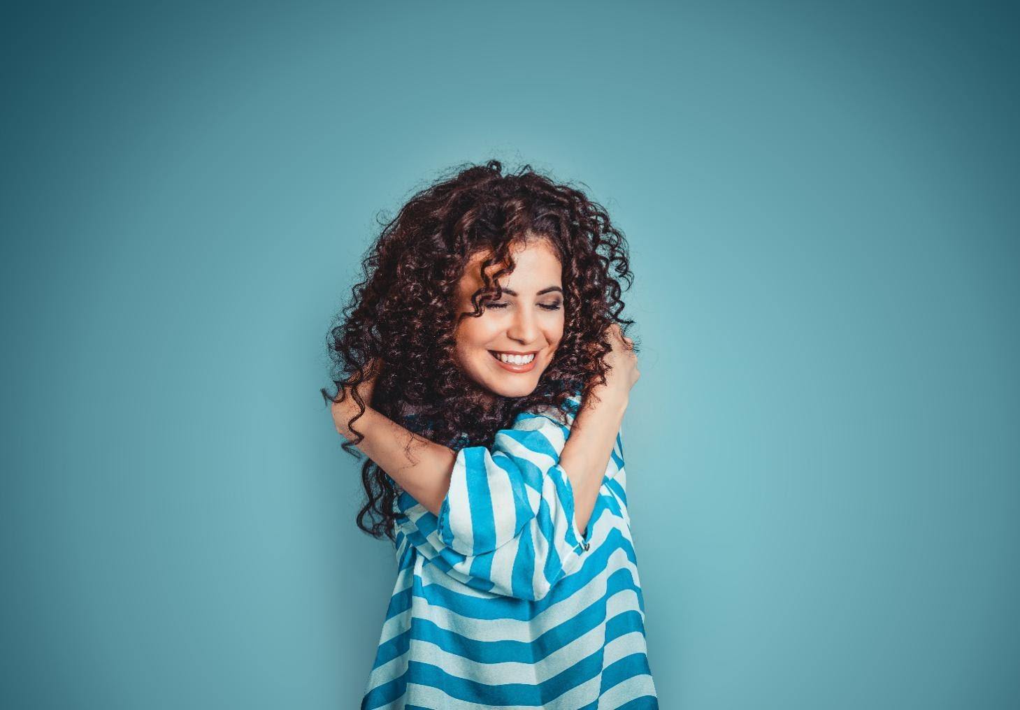 self-confidence booster woman hugging herself against blue wall